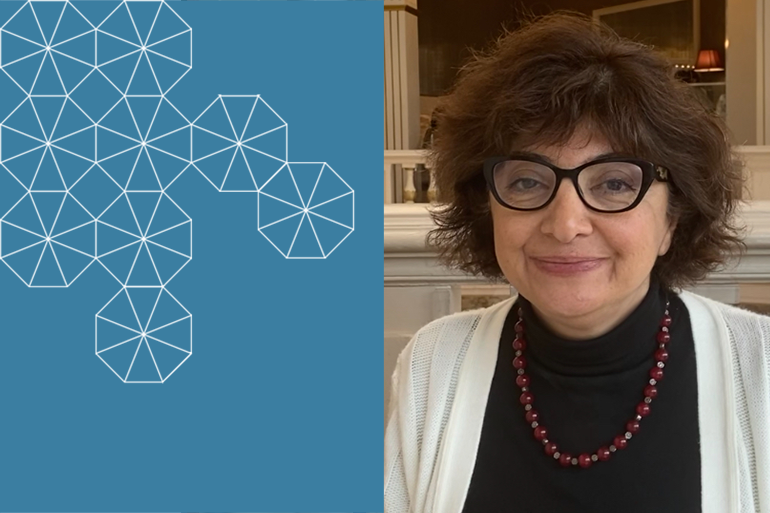 Afsaneh Yavari, smiling in glasses, wearing a dark blouse and white sweater with beads
