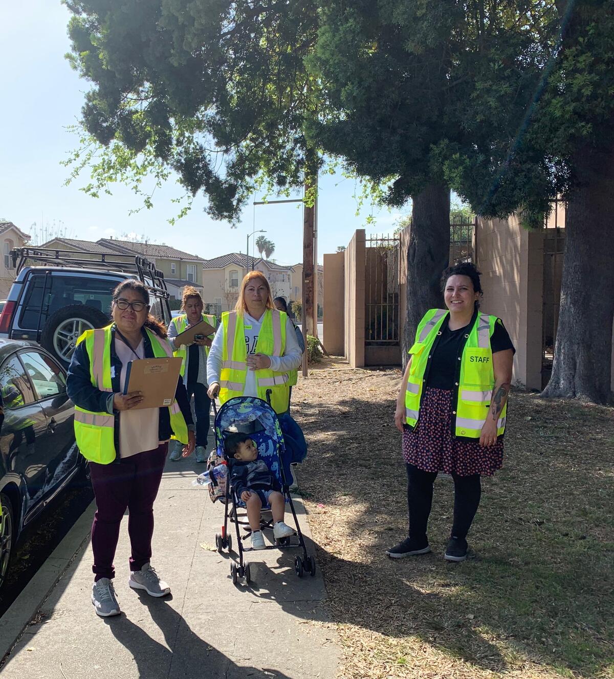 A group of people wearing high visibility vests are pictured during a walking audit, there is a child in a stroller in the middle of the photo