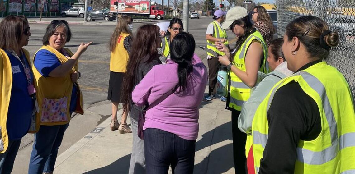 A group of adults wearing safety vests participate in a walking and biking assessment.
