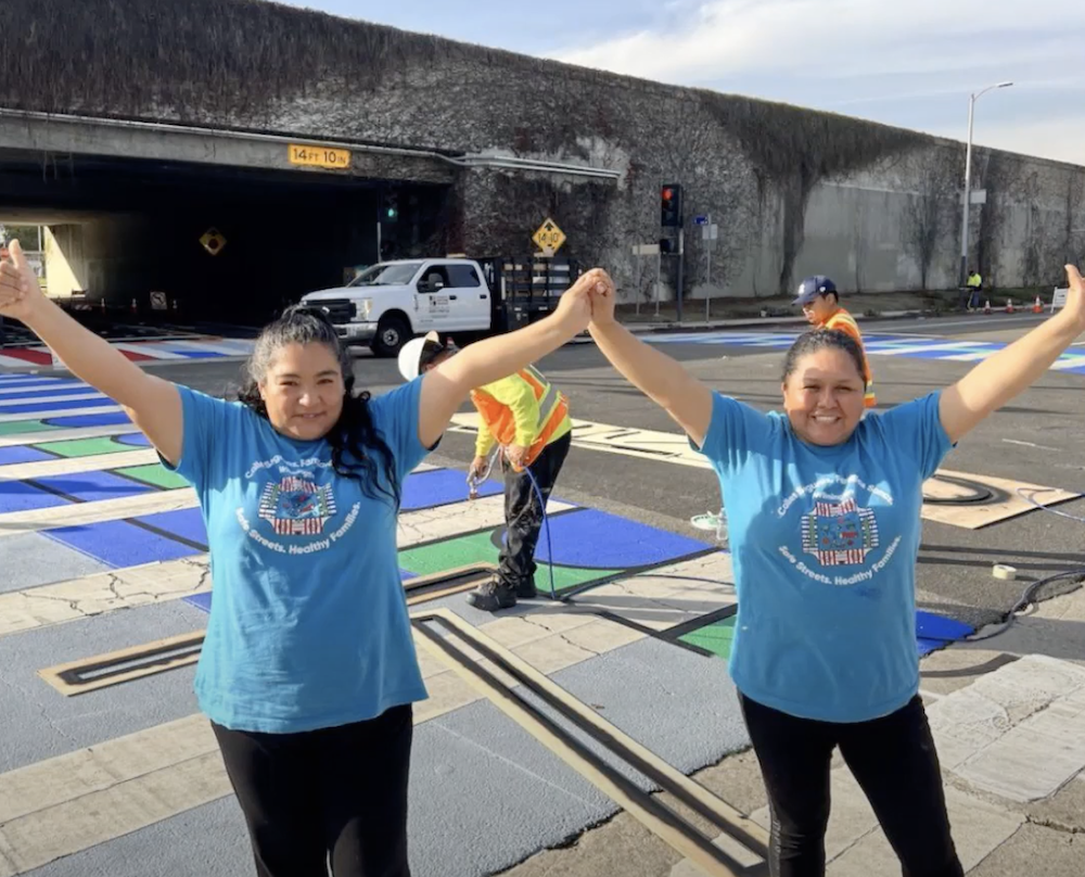Los Angeles Walks Promotoras Leads Gaby Segovia and Nancy Cid raising their arms celebrating a decorative crosswalk 