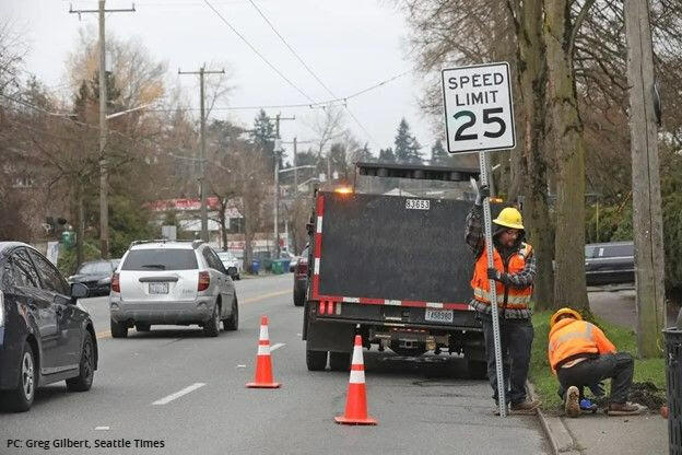 Two construction workers install a 25 MPH speed limit sign on the sign of the road.