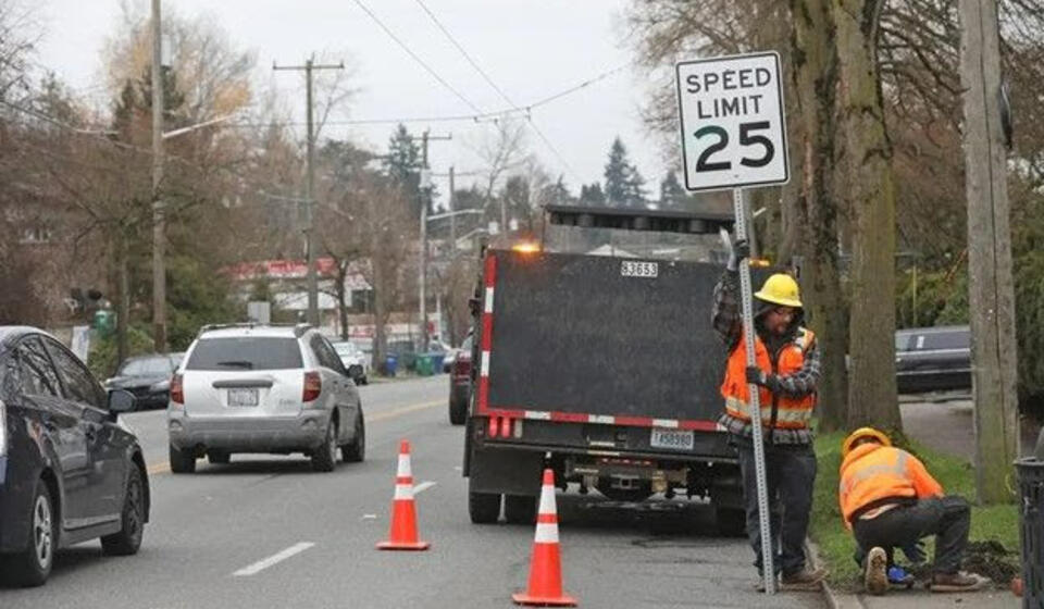 Two workers installing a speed limit sign for 25 mph