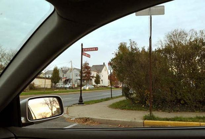 Image of a car at an intersection. The view of the driver is obstructed by bushes. 
