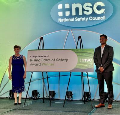 NSC President Lorraine Martin and Praveen Vayalamkuzhi at the NSC Expo holding a sign on stage congratulating the Rising Stars of Safety Award recipients