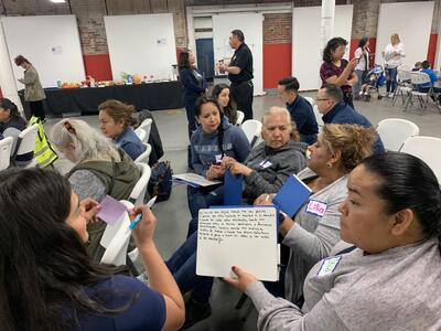 A group of people are huddled together while sitting, one person is pictured holding a piece of paper to discuss potential safety projects for the neighborhood